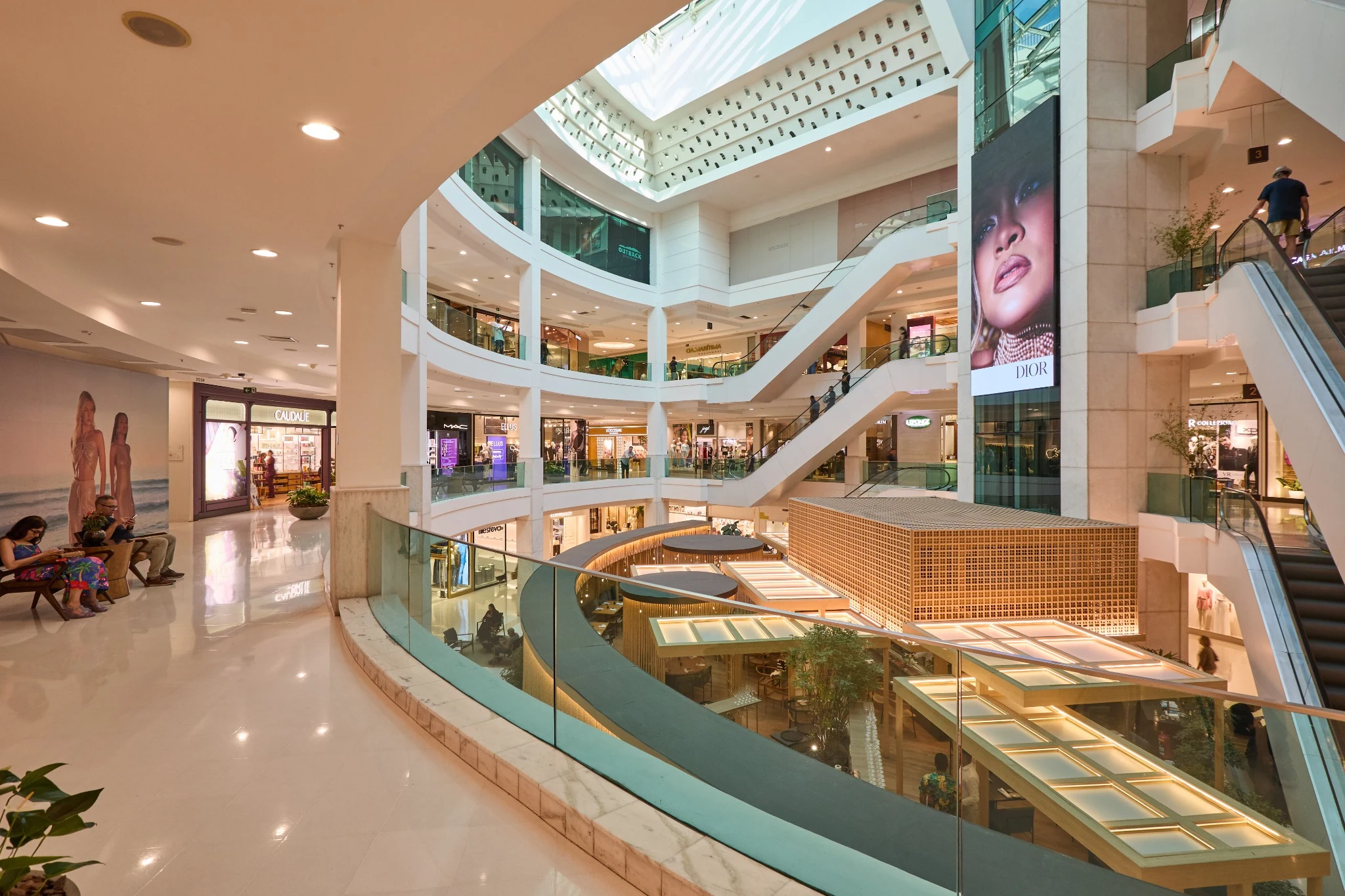 Shopping centre atrium with curved balconies and a glass roof.